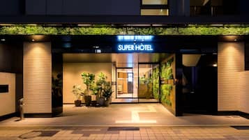 The entrance of a hotel with a sign reading 'SUPER HOTEL'. There are potted plants outside the entrance.