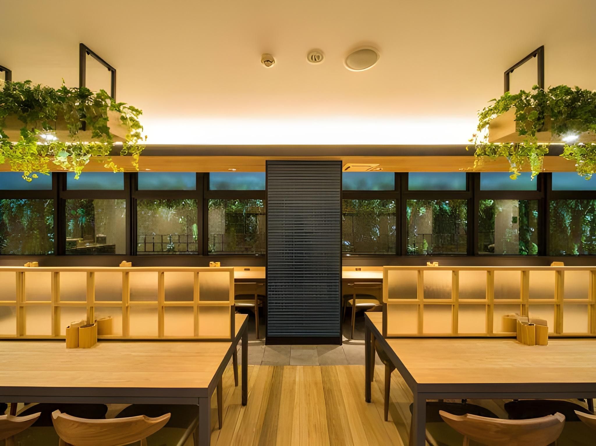 A modern interior with a central black partition, wooden tables, and chairs, and green plants hanging from the ceiling.