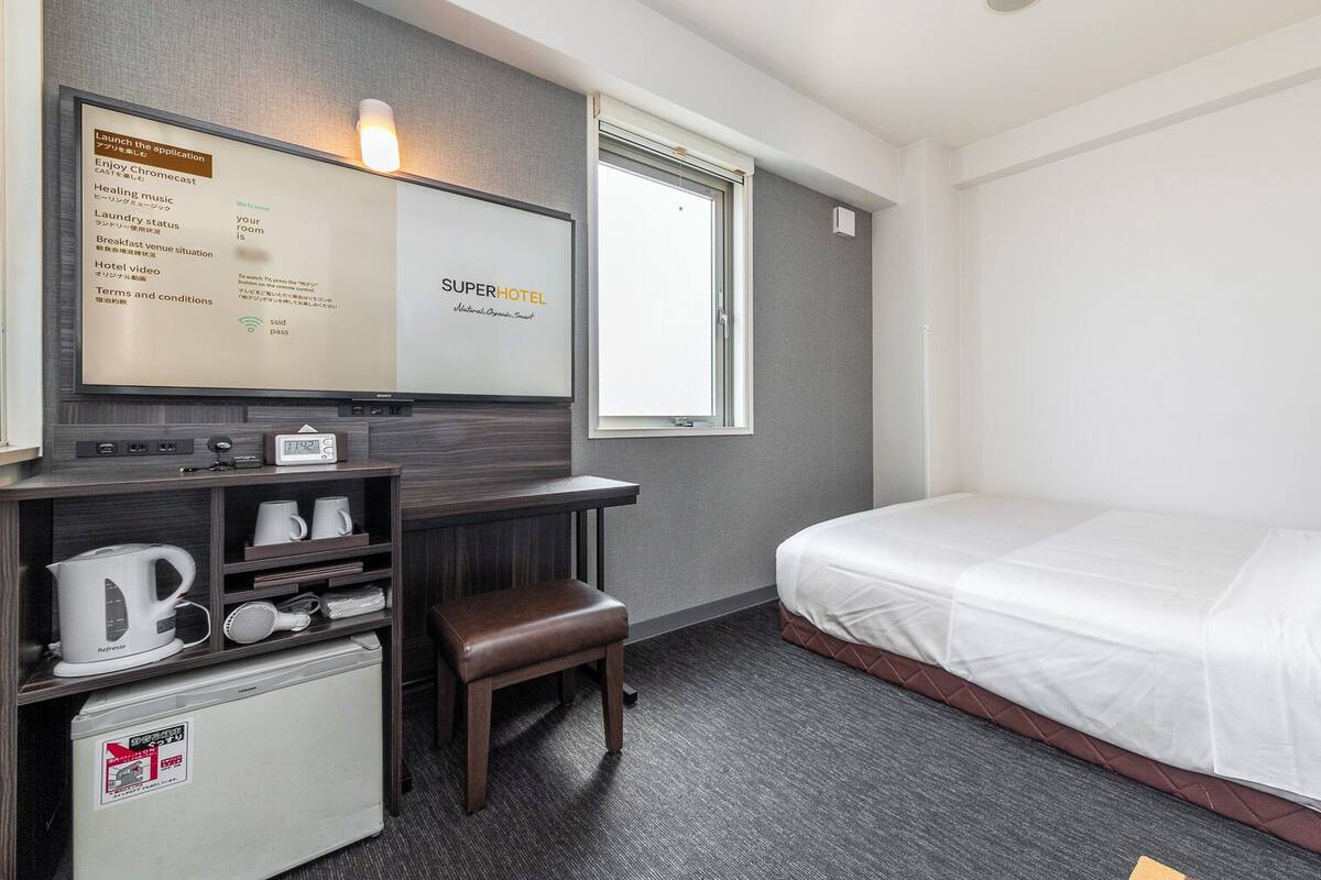 Una habitación de hotel con una cama, un escritorio con computadora, una cafetera y un refrigerador pequeño.