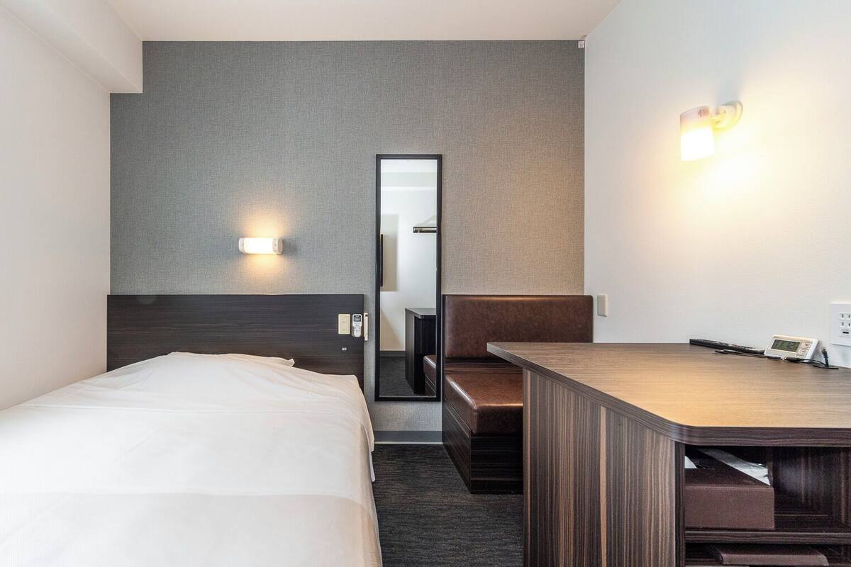 Una habitación de hotel con cama, escritorio, espejo y luz en la pared.