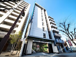 Un edificio moderno de varios pisos con una entrada destacada, grandes ventanales y un cielo despejado.