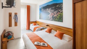 Quarto de hotel com duas camas, cabeceira de madeira, uma janela grande com cortinas, televisão na parede e um quadro de uma cidade costeira.