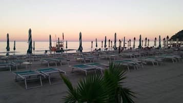 Een privéstrand, ligstoelen aan het strand, parasols, een strandbar