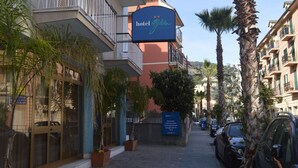 Hotel com placa, plantas em vasos e carros estacionados na rua.