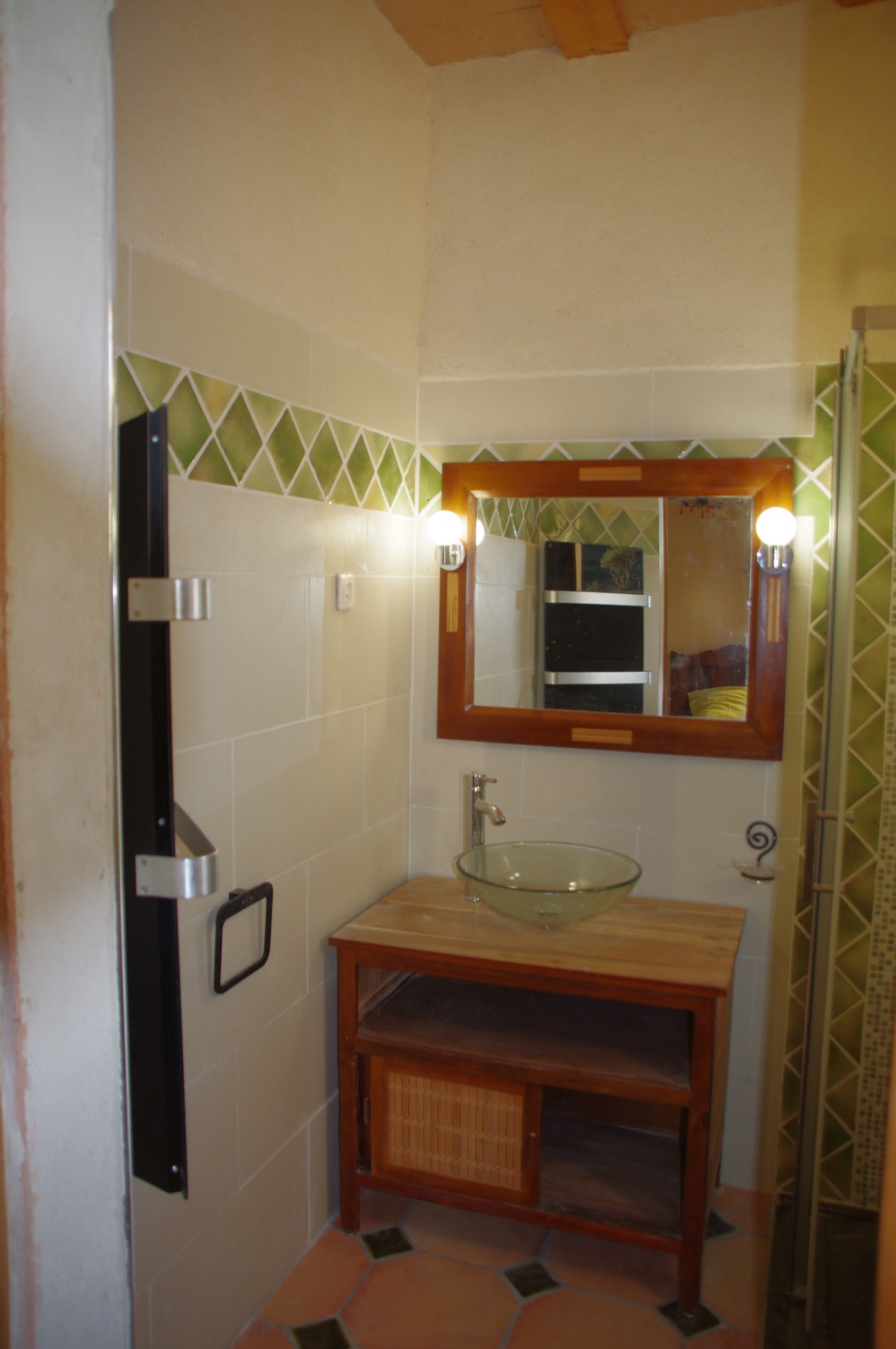 Un baño con lavamanos de vidrio, tocador de madera y espejo con luces.