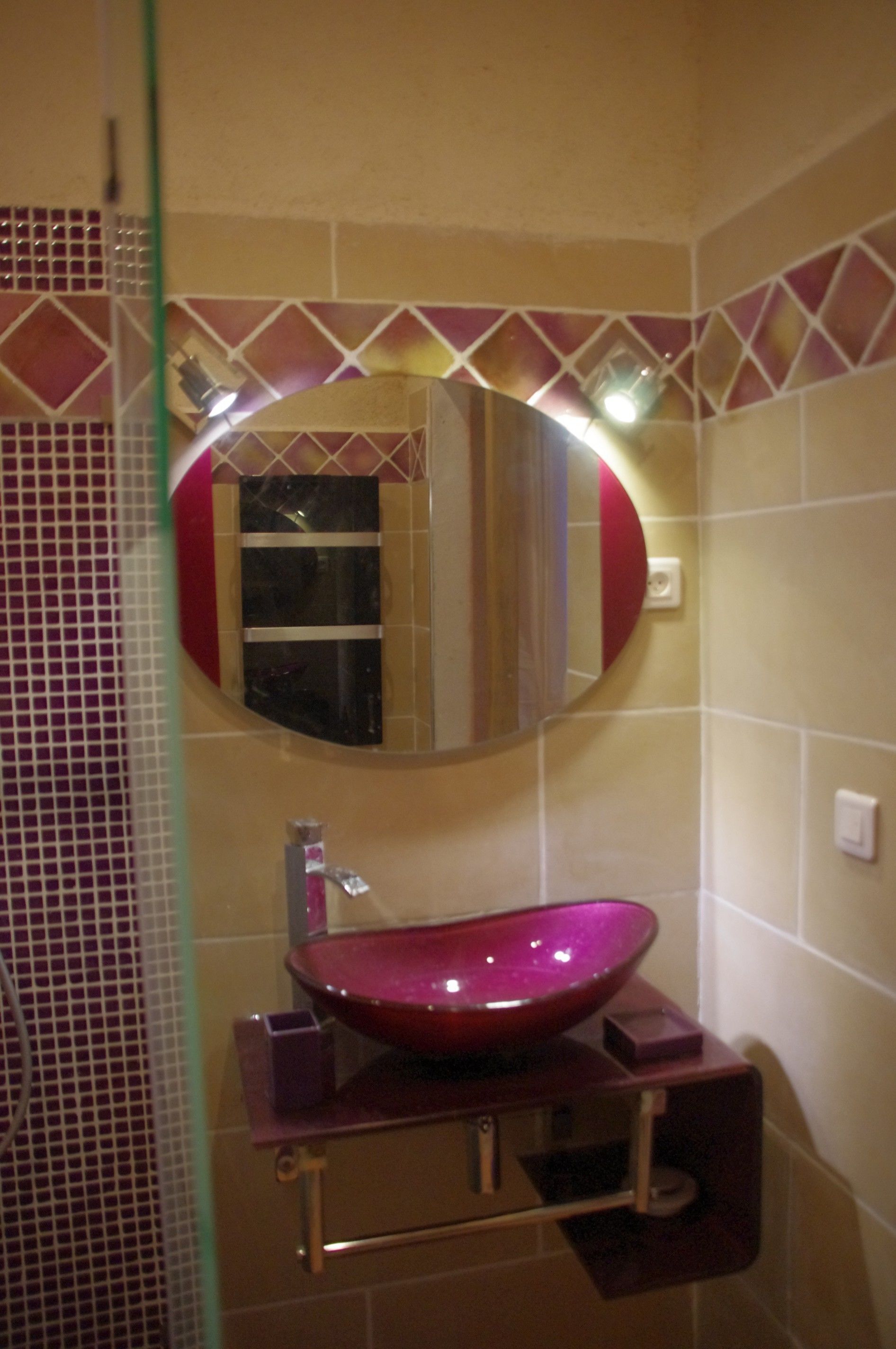 Ein Badezimmer mit einem runden Spiegel, einem roten Waschbecken und einer gefliesten Wand.