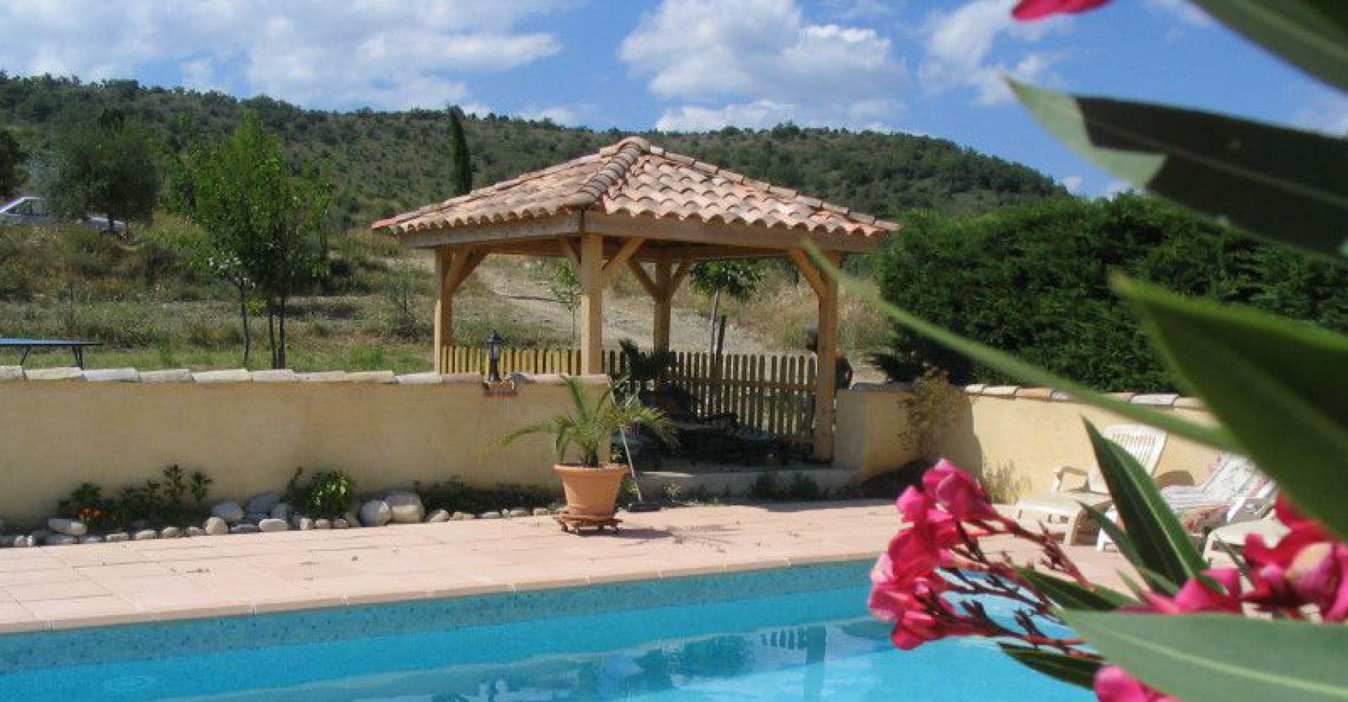 A pool area with a wooden gazebo, a potted plant, and a view of a hilly landscape.