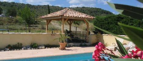 A pool area with a wooden gazebo, a potted plant, and a view of a hilly landscape.