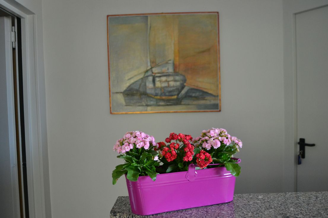 A bathroom with a granite countertop, a purple flower pot, and a painting of a sailboat on the wall.