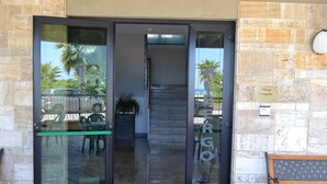 A hotel entrance with a glass door, a bench outside, and a stone wall with a plaque. - Hotel Quaglia (Roseto degli Abruzzi)
