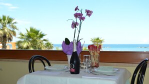A table set for dining with a bottle of wine, a vase with purple flowers, and a view of the ocean. - Hotel Quaglia (Roseto degli Abruzzi)