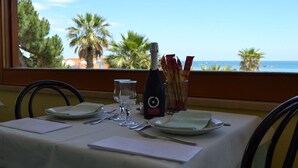 A table set for two with a bottle of champagne, glasses, and cutlery, overlooking a beach with palm trees. - Hotel Quaglia (Roseto degli Abruzzi)
