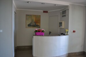 A reception area with a white reception desk, a painting on the wall, a fire alarm, and a fire extinguisher.