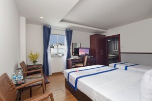 A hotel room with two beds, a desk, a chair, a TV, and a window with curtains.