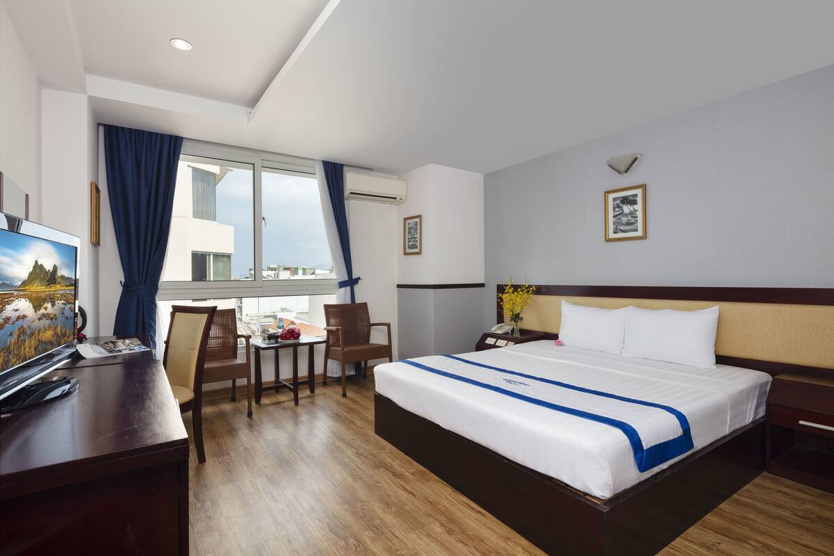 A hotel room with a large bed, a desk with a computer, a chair, and a window with curtains.