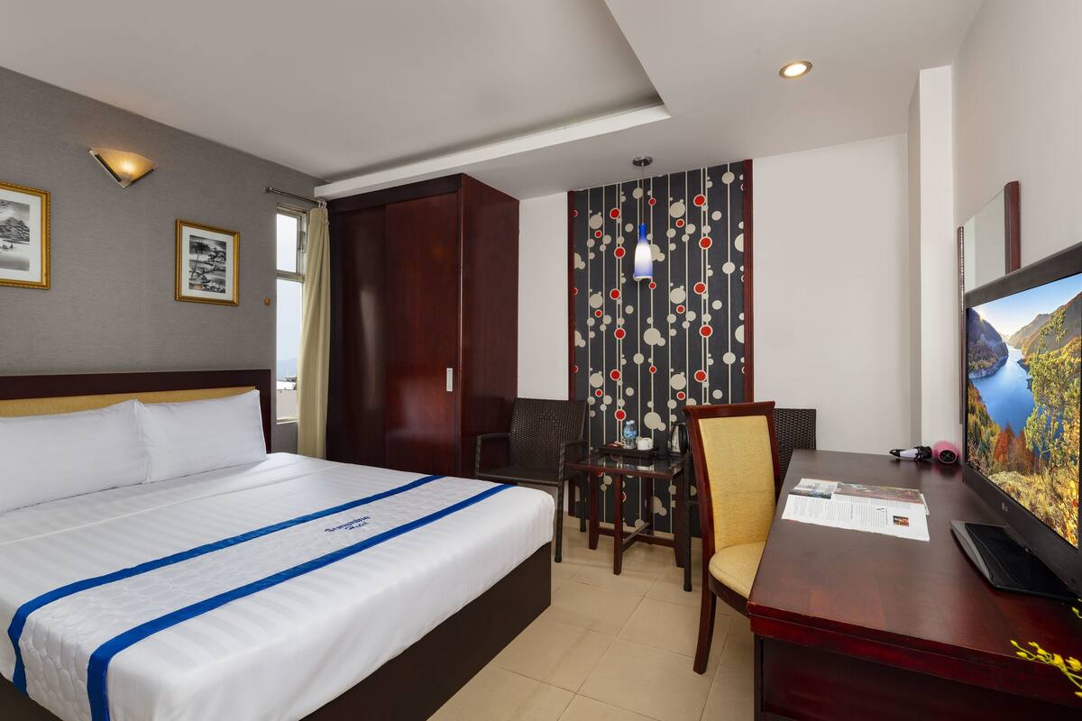 A hotel room with a large bed, a desk with a computer, a chair, and a TV.