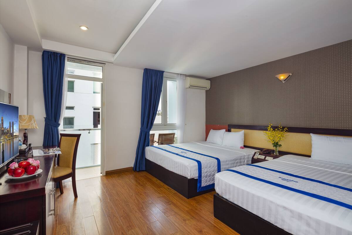 A hotel room with two beds, a desk with a lamp, a chair, and a view of the outside.