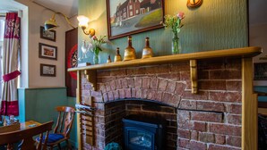 A brick fireplace with a mantel shelf, a dining area with wooden furniture, and a framed picture on the wall. - The Beacon Inn (Stonehouse)
