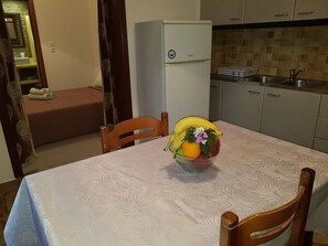 Ein Essbereich mit einem Tisch für zwei Personen, einem Kühlschrank, einer Spüle und einem Bett im Hintergrund.