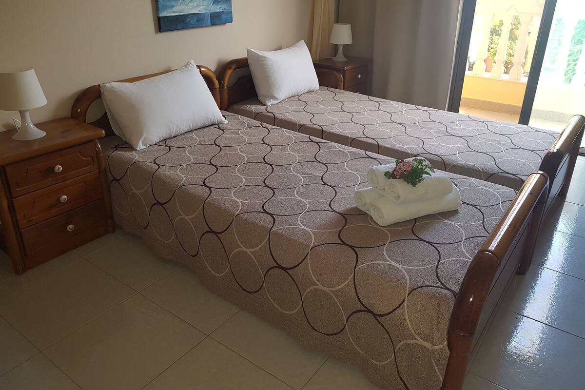 Une chambre d’hôtel avec deux lits, chacun recouvert d’une couvre-lit à motifs, une table de chevet avec une lampe et un tableau accroché au mur.