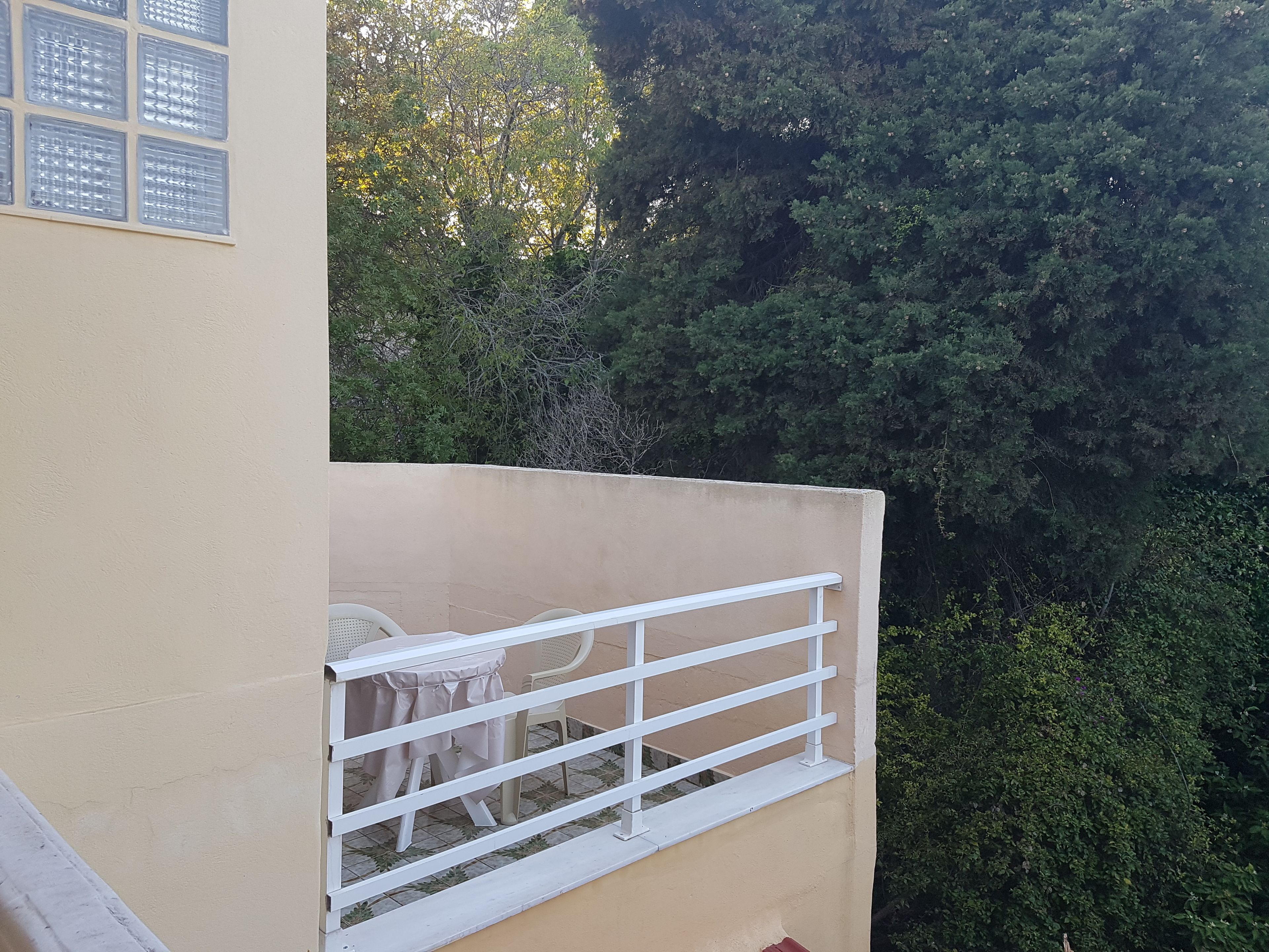 Ein Balkon mit weißer Brüstung, einem kleinen Tisch mit weißem Tuch und einem Stuhl.