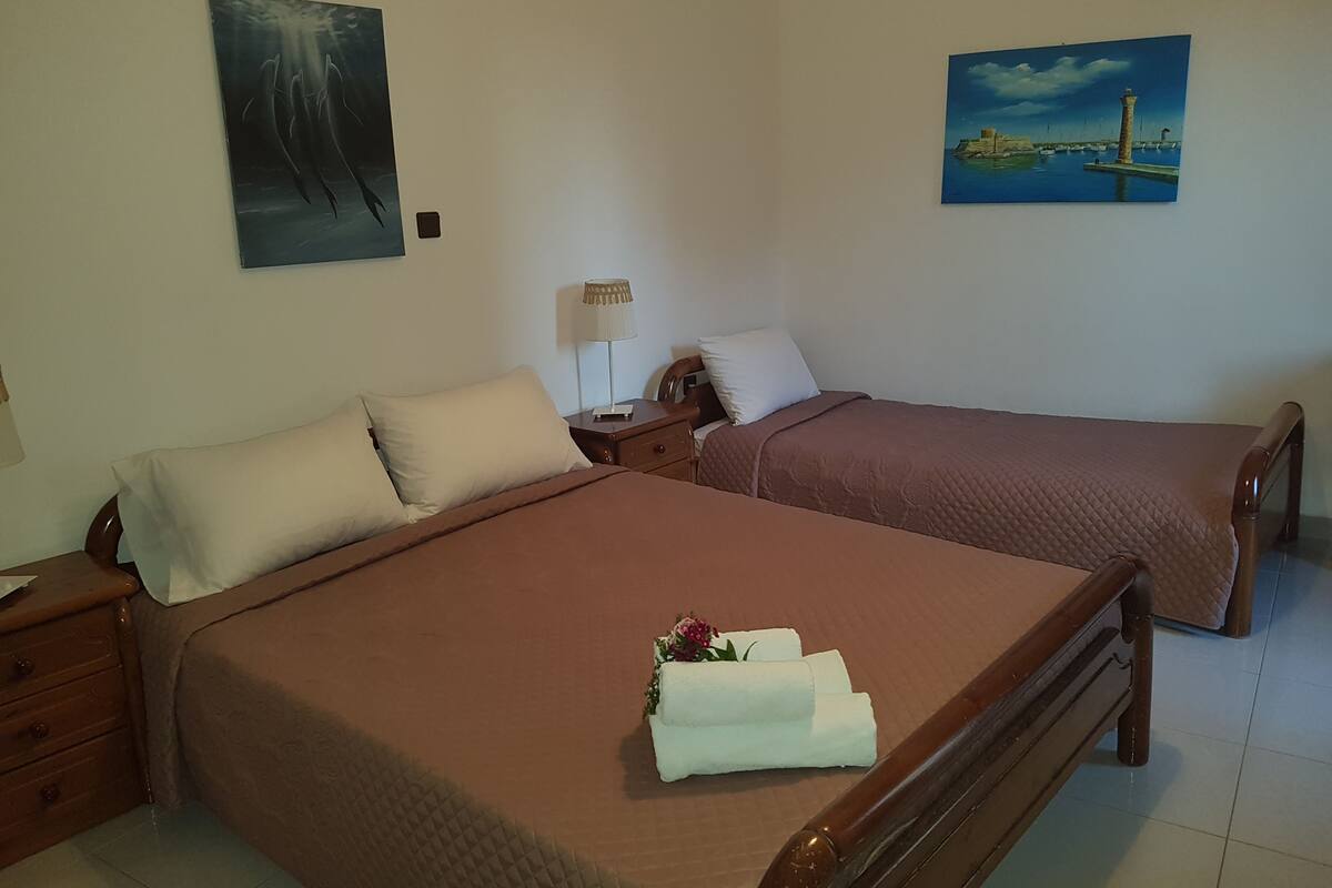 Une chambre d’hôtel avec deux lits, une table de chevet, une lampe et deux tableaux accrochés aux murs.