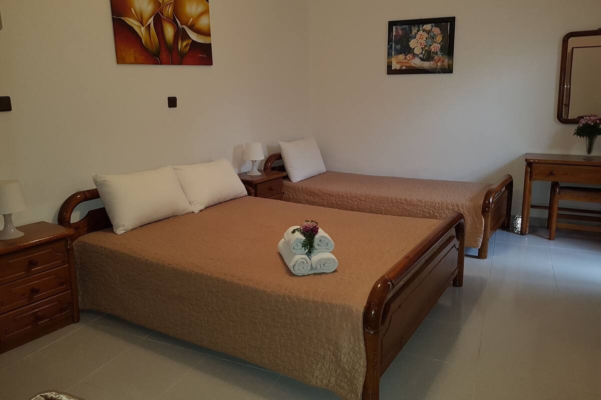 Une chambre d’hôtel avec deux lits, une table de chevet, une commode, un bureau et deux tableaux accrochés aux murs.