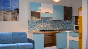 Cozinha compacta com armários azuis, fogão a gás, micro-ondas e um sofá azul na sala.