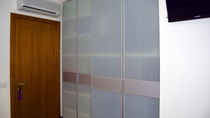Quarto com porta de madeira, ar-condicionado fixado na parede e televisão de tela plana.