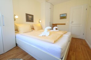 Ein ordentlich bezogenes Bett mit weißen Leinen und dekorativen Kissen, ein Holzboden und ein weißer Kleiderschrank.