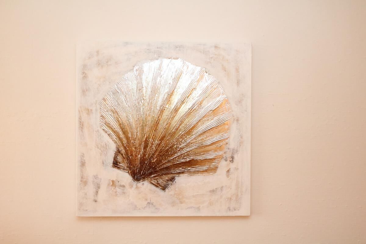 A square artwork with a shell design on a plain wall.
