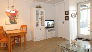 Un soggiorno con un tavolo da pranzo in legno, sedie, un tavolino in vetro, una televisione e mobili contenitori bianchi.