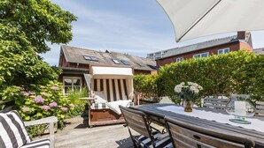 An outdoor patio with a wooden table, striped sofa, and a large umbrella. - The locksmith's shop awarded 5 stars according to DTV (Westerland)