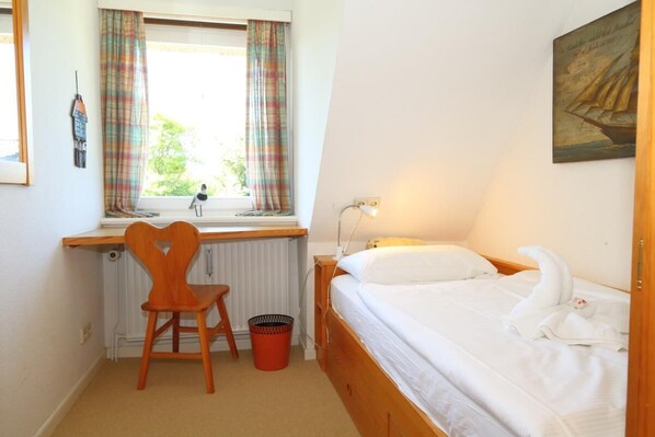 A bedroom with a wooden bed, a desk with a chair, a window with curtains, and a radiator.