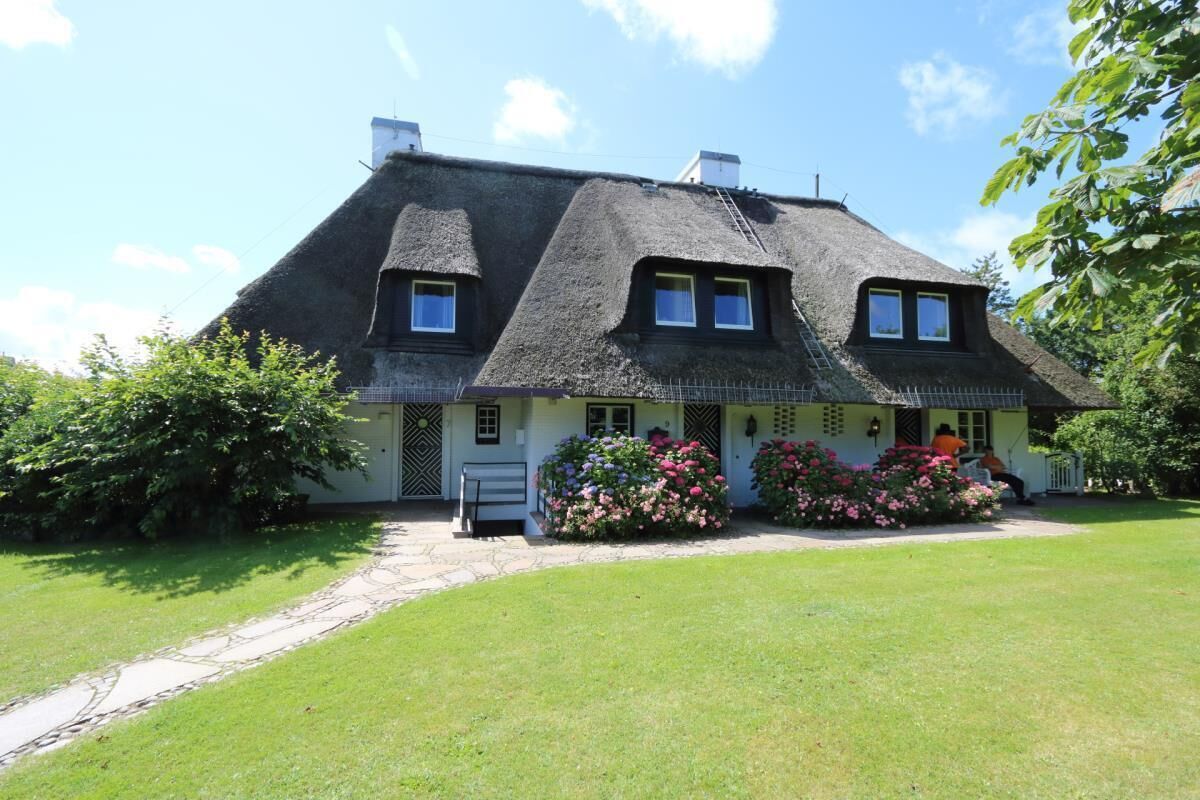 Ein traditionelles Haus mit einem Reetdach, einer Veranda und einem gepflegten Garten.