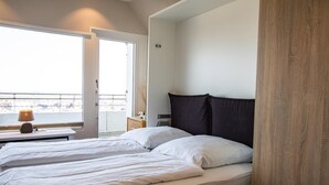 A hotel room with two beds, a window with a view, a bedside table with a lamp, and a wooden headboard. - Metro 335 - with stunning views over the island (Westerland)