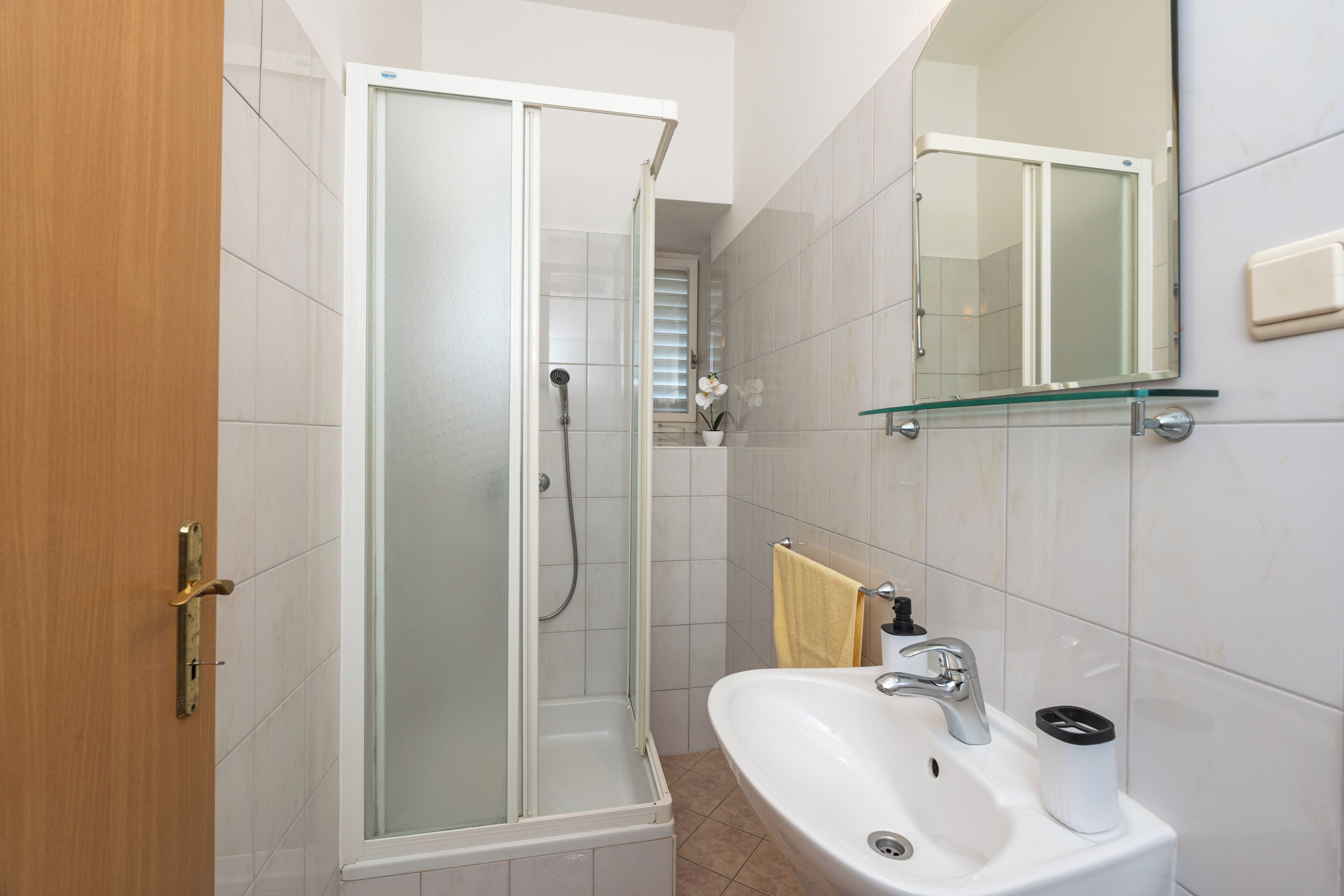Un baño con ducha compartimentada con vidrio, un lavamanos con espejo y un perchero para toallas.