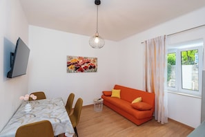 Uma sala de estar moderna com área de jantar, um sofá, uma televisão fixada na parede e uma janela com cortinas.