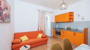 A compact living space with a sofa, dining table, and kitchen area. - Apartment Cecilija - waterfront with sunbeds (Zaton)