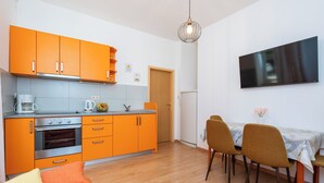 A compact kitchen with orange cabinets, a dining area with two chairs, and a flat-screen TV on the wall. - Apartment Cecilija - waterfront with sunbeds (Zaton)