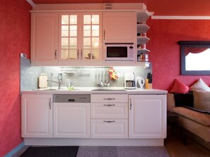 Una cucina con mobili bianchi, un forno a microonde, una macchina da caffè e un lavello.