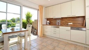 Een moderne keuken met witte kasten, een houten aanrechtblad en een eethoek met een tafel en stoelen.