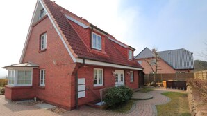Een rode bakstenen woning met schuin dak, een voortuin en een verharde oprit.
