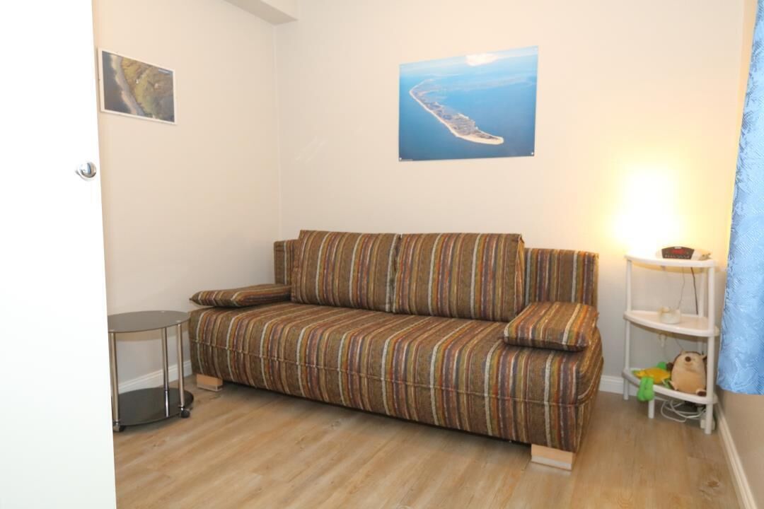 Et hyggeligt, lille værelse med en stribet sofa, et rundt bord og en reol med legetøj.