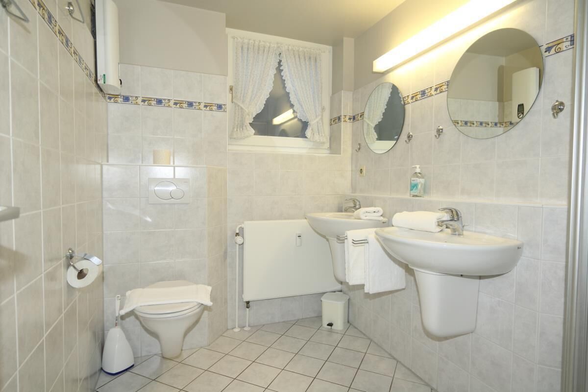 Une salle de bain équipée de toilettes, d’un bidet, d’un lavabo et de miroirs.