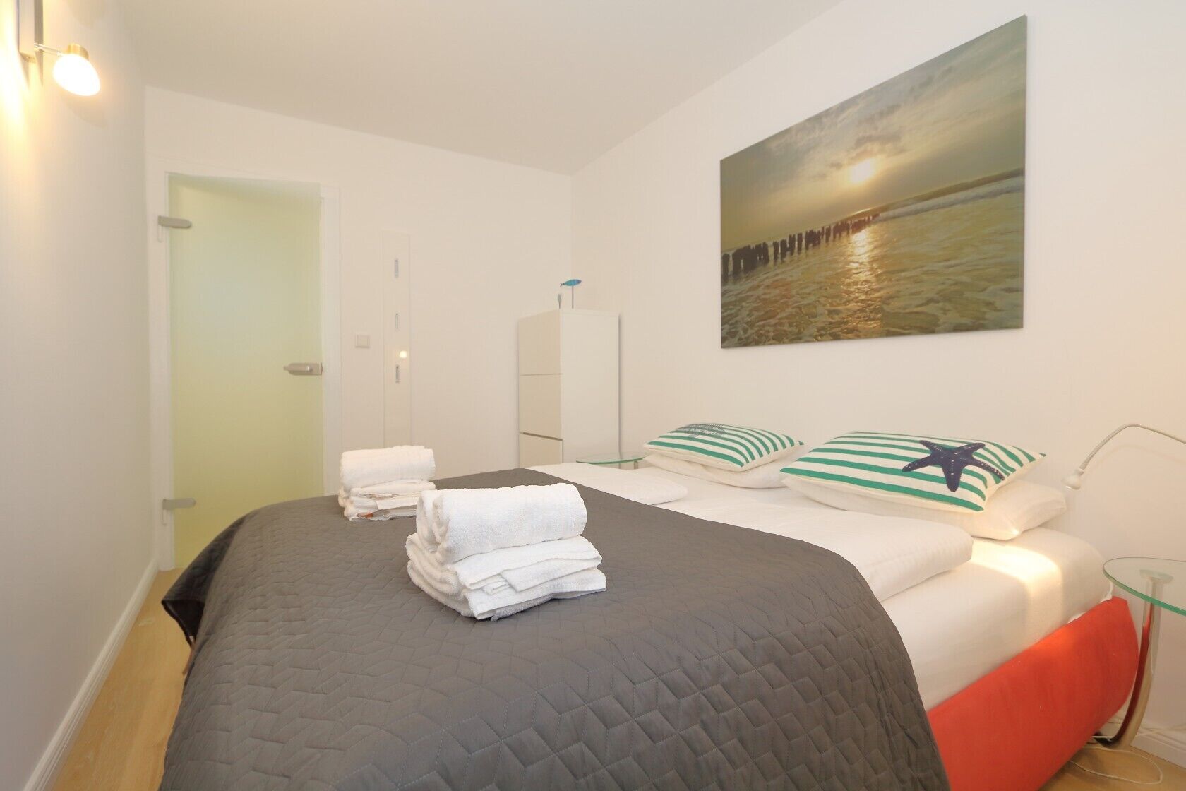 Een hotelkamer met een bed, een schilderij van een ondergaande zon boven water, en een deur naar een andere kamer.
