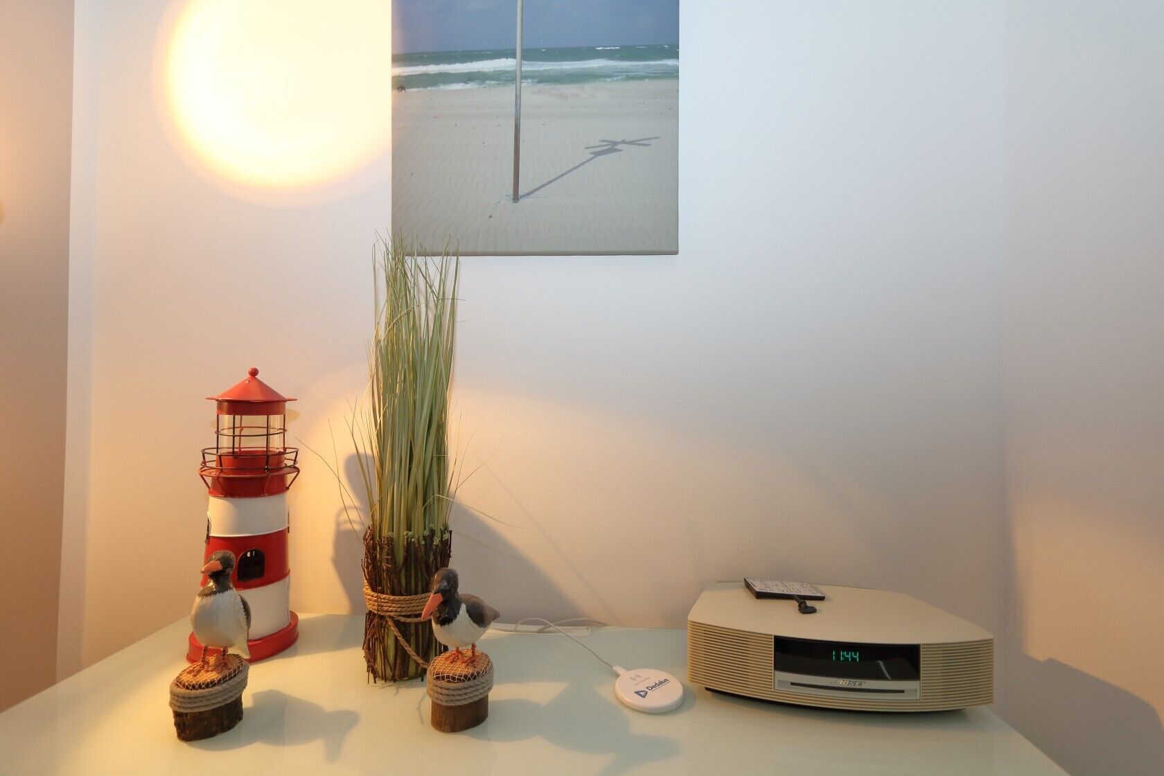 A room with a lighthouse model, a plant, a small bird figurine, and a radio on a table.