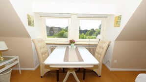 Un comedor con una mesa blanca, dos sillas color beige, un florero con flores y vistas amplias a través de grandes ventanas.