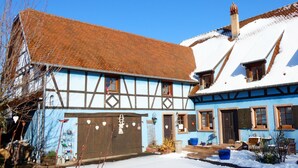 Une maison traditionnelle à colombages, avec un toit enneigé et une façade bleue.