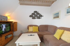 A living room with a television, a white coffee table, a brown sofa with yellow cushions, and a wall decal of fish. - Welcome to the Syltnest apartment in Munkmarsch. (Munkmarsch)